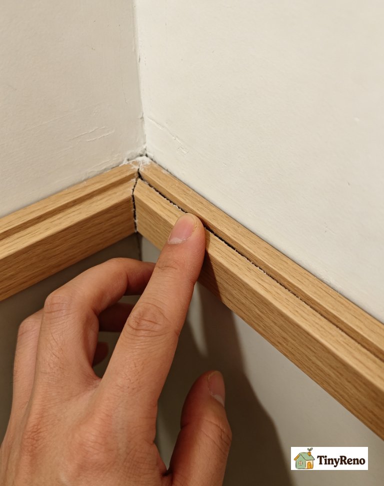 Renter checking a trim seam; pressing trim to see if it flexes, observing gap width difference between cold and warm conditions to pick spackle or caulk.