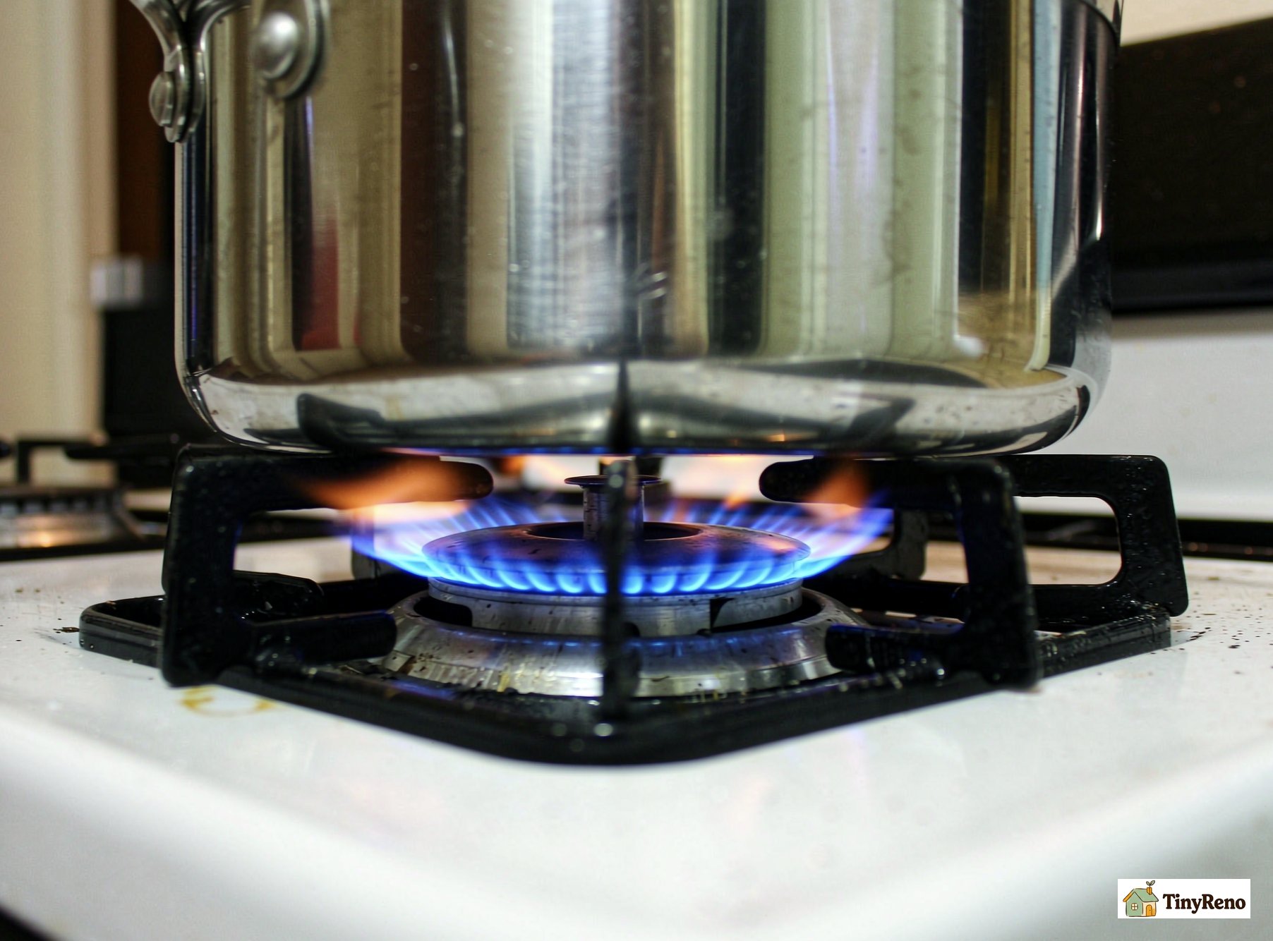 A gas stove burner with a lit flame under a metal pot in a kitchen